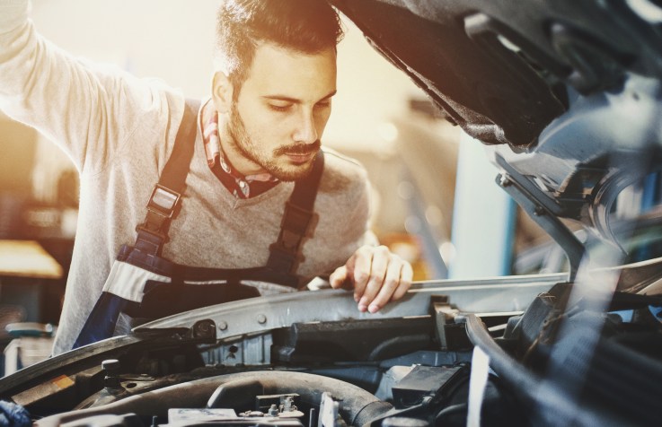 Closeup of mechanic in engine bay, preparing a car for the summer season.
